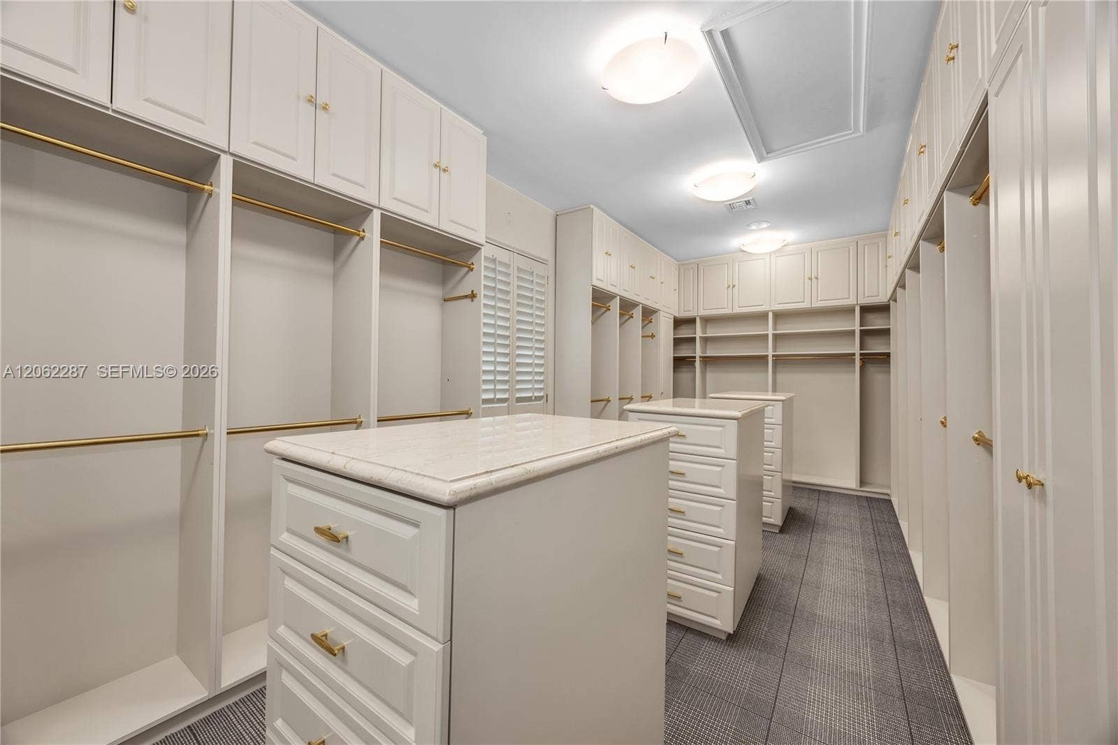 Custom built-in cabinetry featuring white shaker-style doors, dual islands with stone-composite countertops, matte gold hardware, tiered shelving, and hanging rods