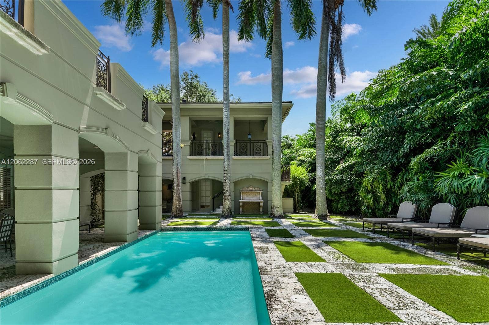 Stucco exterior featuring arched architectural detailing, two-story covered loggias with wrought-iron railings, stone-tiled pool deck, and a rectangular swimming pool