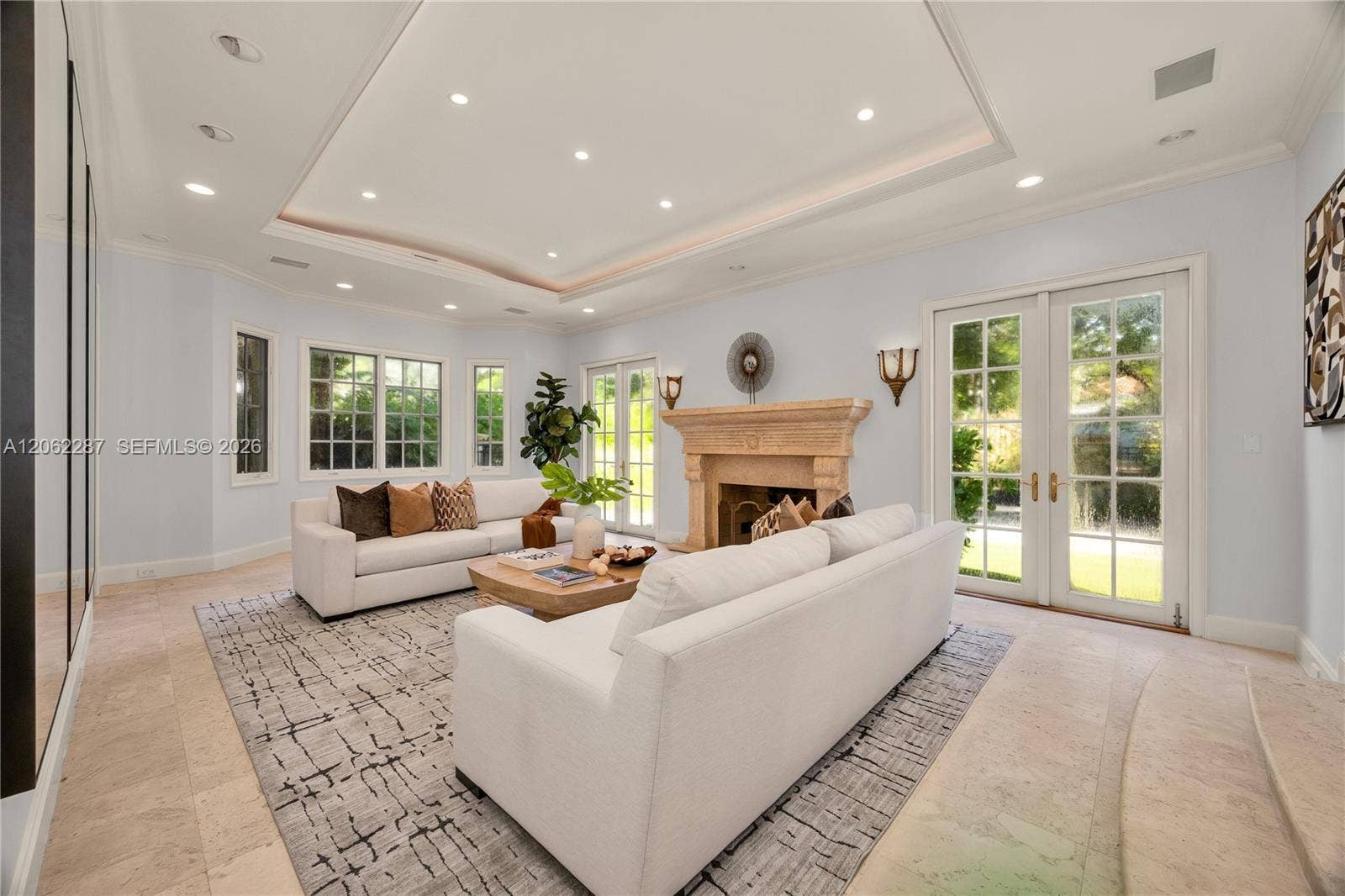 Living area featuring stone flooring, a decorative stone fireplace mantle, recessed tray ceiling, and multiple sets of glass-paned French doors