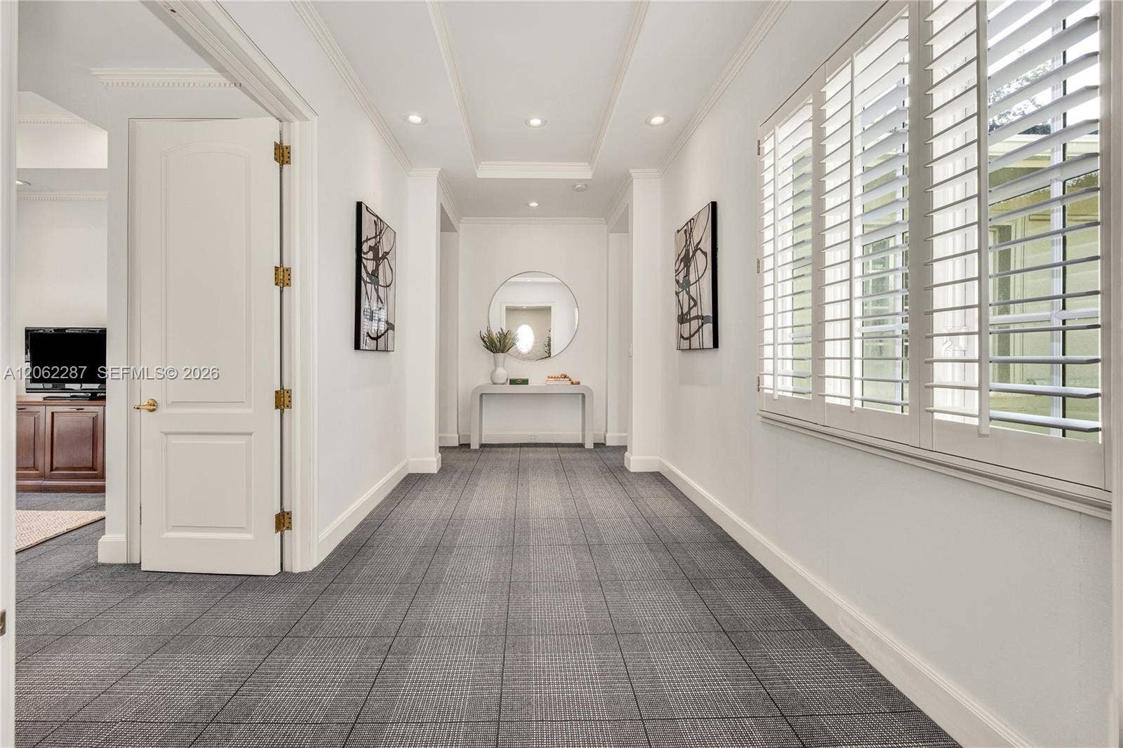 Hallway featuring recessed ceiling lighting, tray ceiling details, plantation shutters, and patterned carpeting