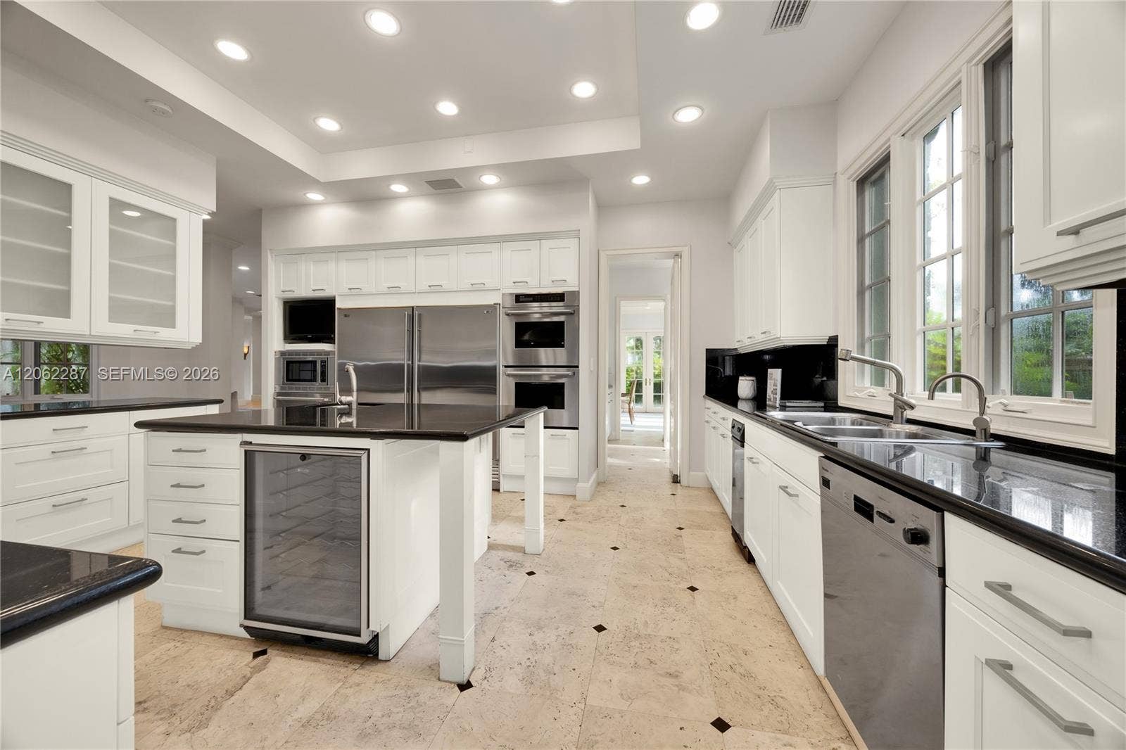 Kitchen featuring white cabinetry, dark stone countertops, stainless steel appliances, a central island with a built-in beverage refrigerator, and stone tile flooring with decorative inlay accents