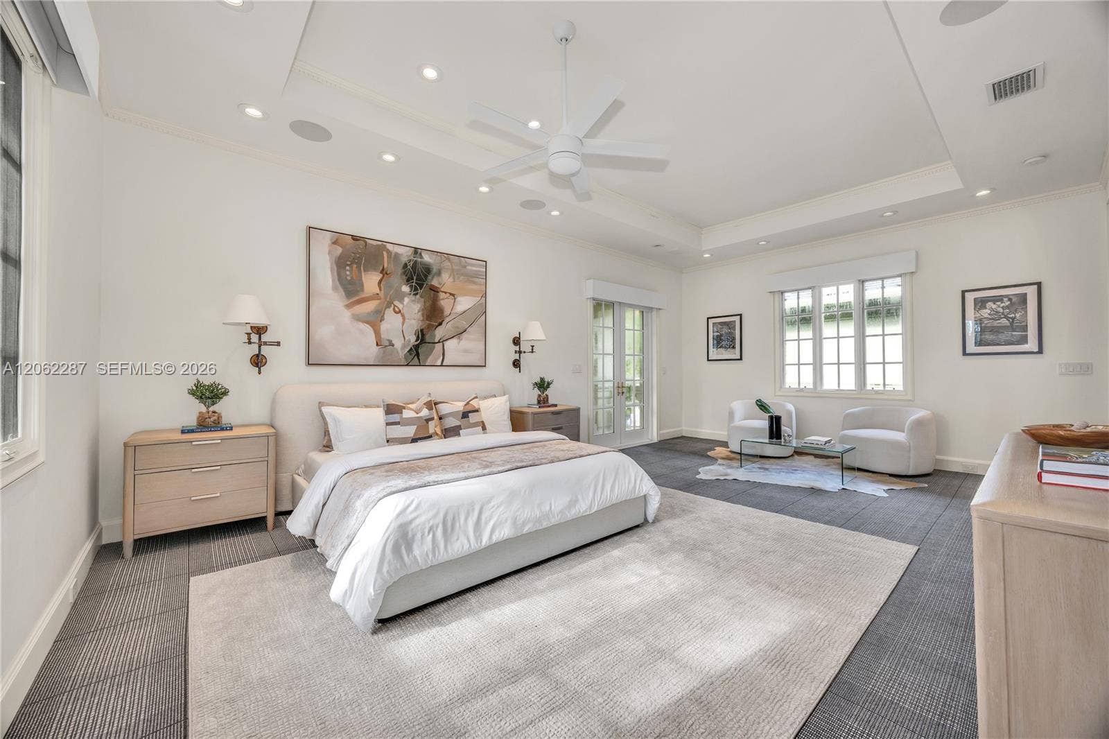 Spacious room featuring a recessed tray ceiling, white multi-blade ceiling fan, integrated recessed lighting, grid-pattern windows, and multi-light French doors