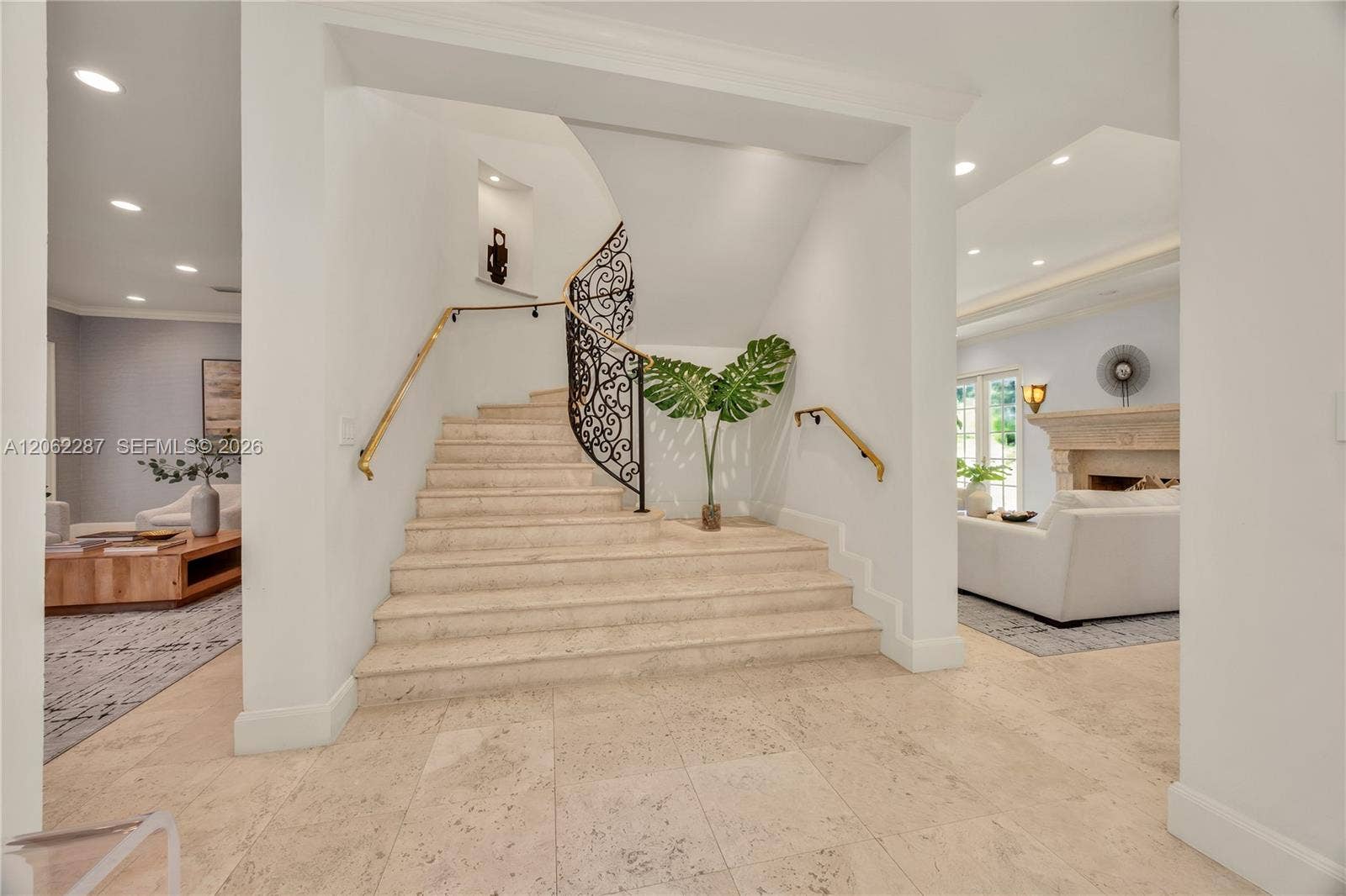 Grand foyer featuring a stone staircase with ornate iron railing, brass handrails, recessed wall niche, and natural stone flooring with recessed lighting