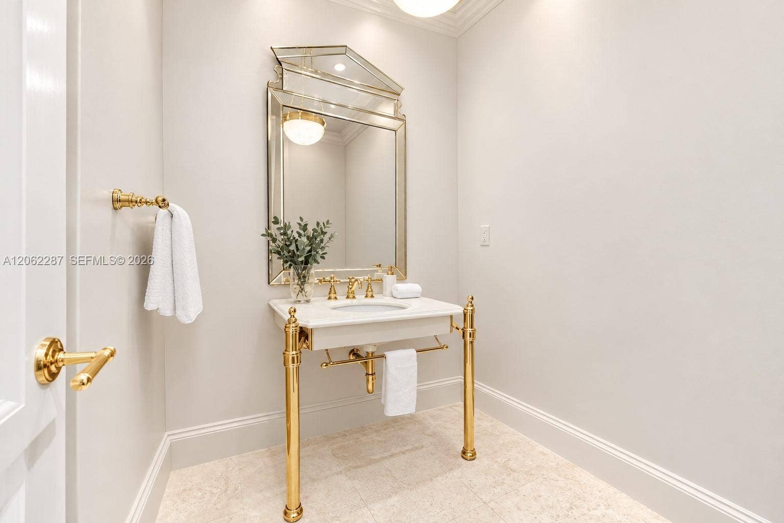 Console-style sink with stone countertop, polished gold-tone metal legs, decorative framed mirror, and coordinating gold-tone faucet and hardware