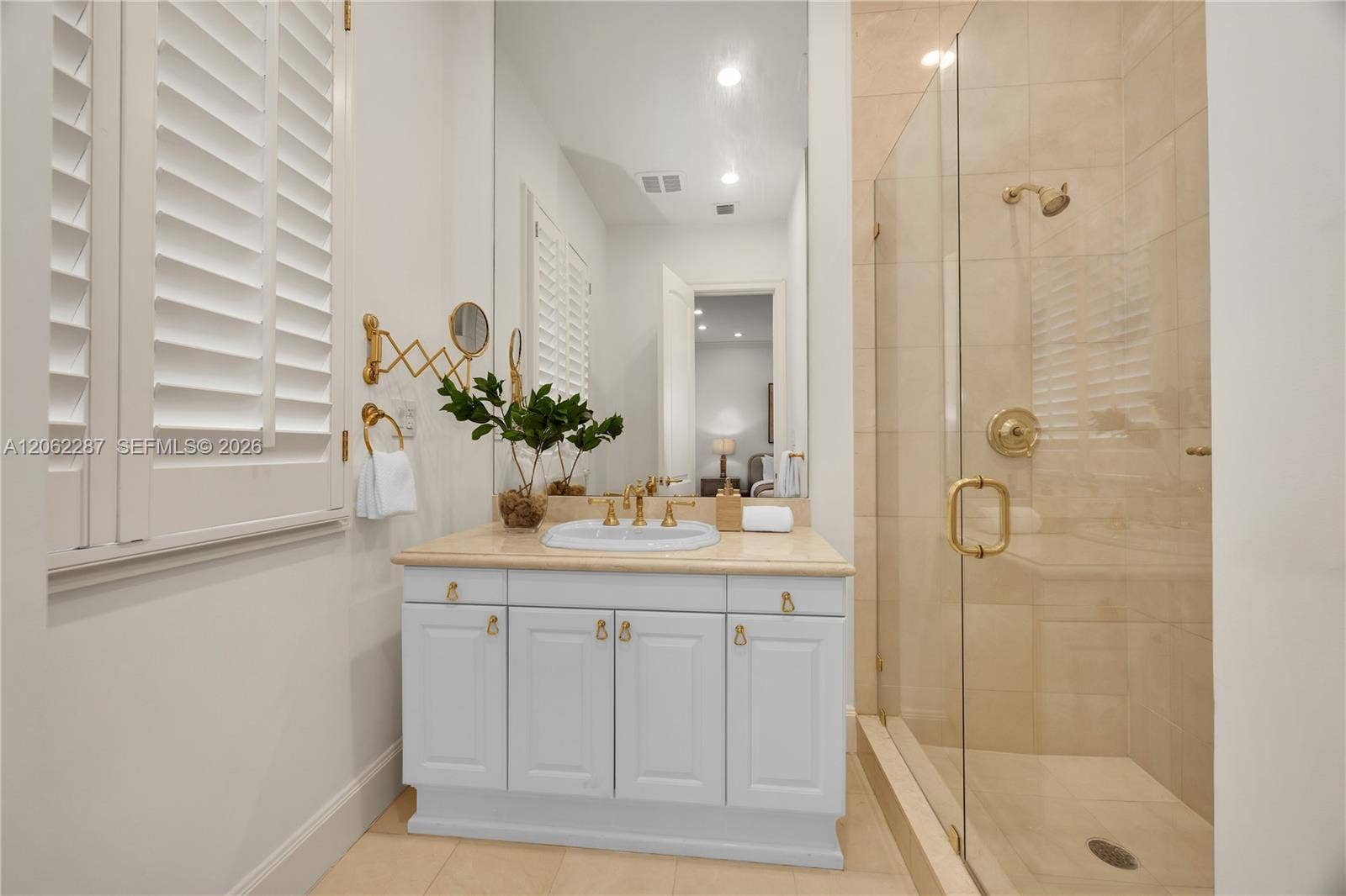 Bathroom featuring white cabinetry, stone-surface countertop, undermount sink, brass-finish fixtures, and a glass-enclosed shower with floor-to-ceiling tile
