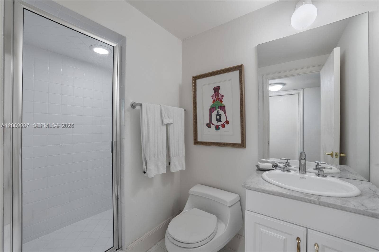 Staff Suite: Bathroom featuring a stone-top vanity with an integrated oval sink, chrome widespread faucet, frameless glass-enclosed shower with white wall tile, and a wall-mounted mirror