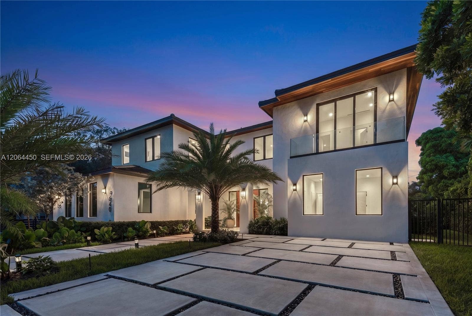 Twilight view of the residence with architectural lighting and palm lined grounds