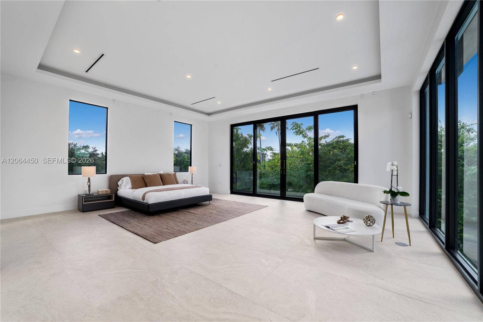 Serene bedroom with tray ceiling and walls of glass framing the treetops