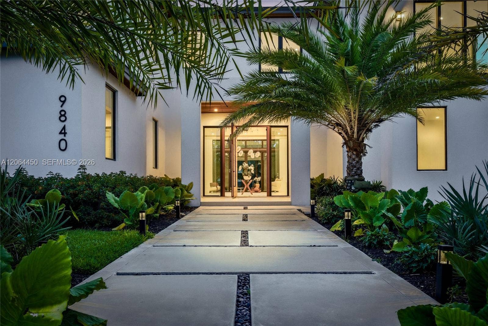 Welcoming entry walkway lined with lush tropical landscaping leading to the front door
