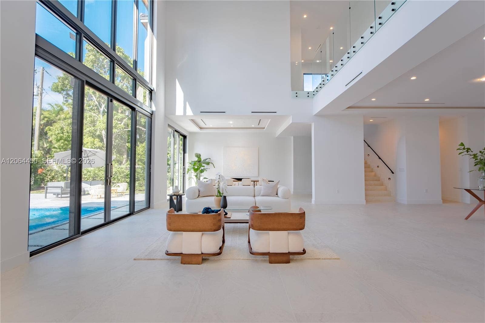 Great room with floor to ceiling windows framing the pool and tropical landscaping