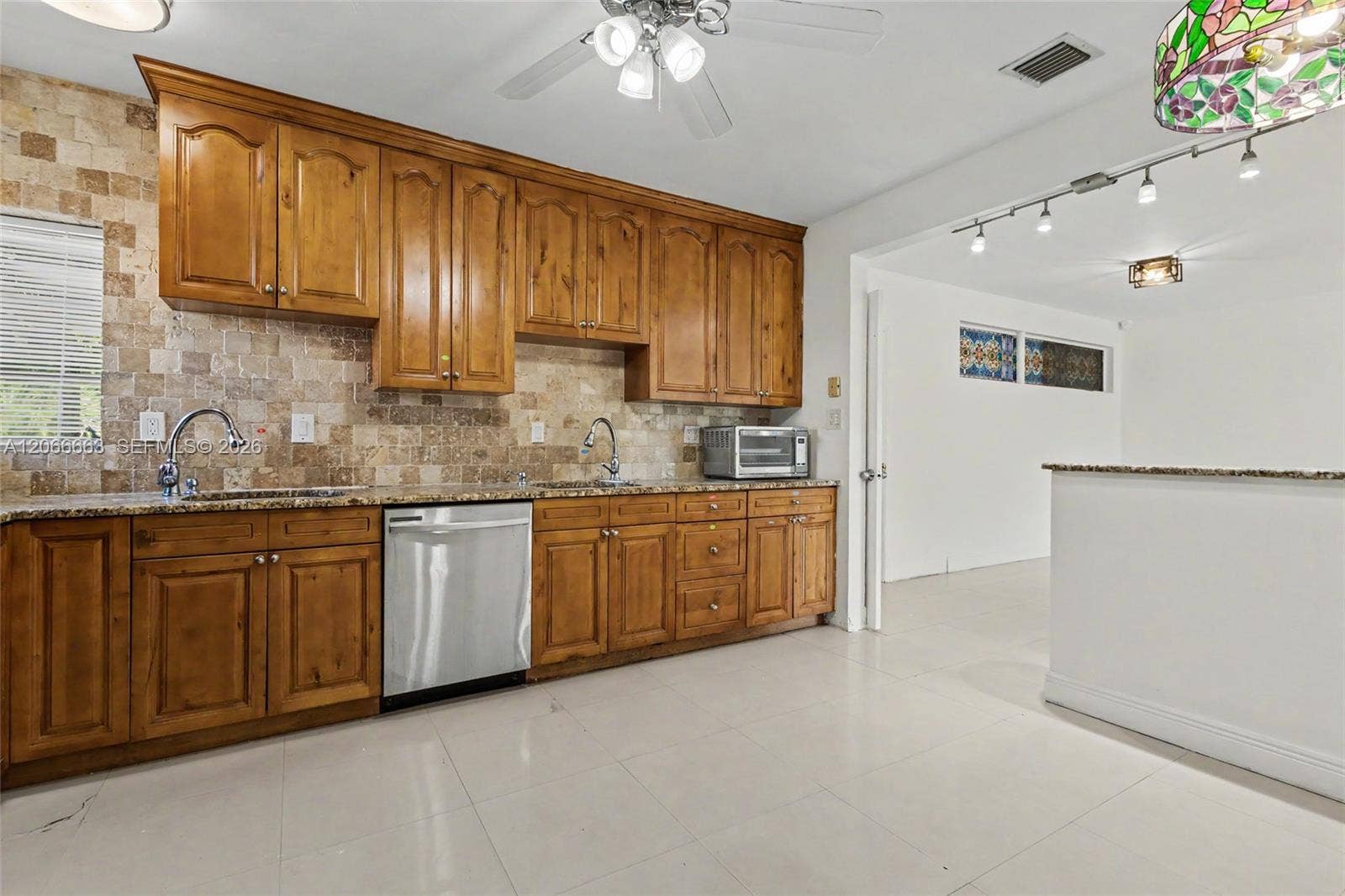 1191 NE 175th Street, North Miami Beach, FL 33162 Kitchen featuring wood cabinetry, natural stone backsplash, stone countertops, a stainless steel dishwasher, and tile flooring
