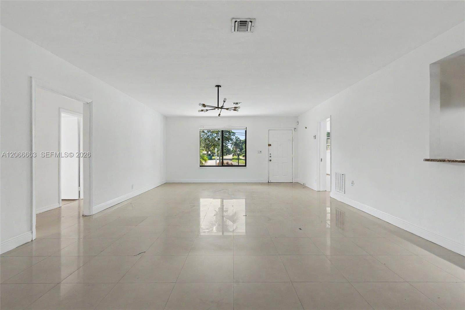 1191 NE 175th Street, North Miami Beach, FL 33162 Open-concept interior featuring large-format tile flooring, neutral wall finishes, a multi-arm modern chandelier, and a prominent exterior window