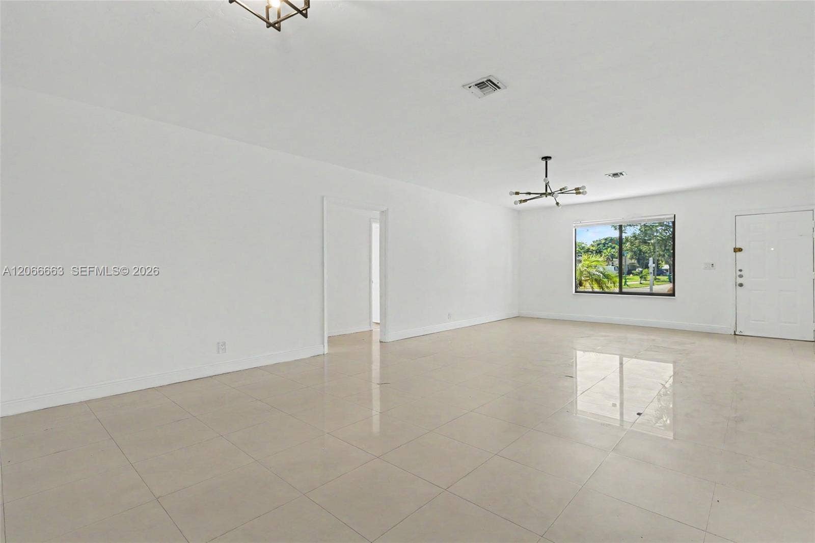 1191 NE 175th Street, North Miami Beach, FL 33162 Open interior space featuring light-colored tile flooring, neutral wall finishes, a multi-arm modern light fixture, and large-paned window