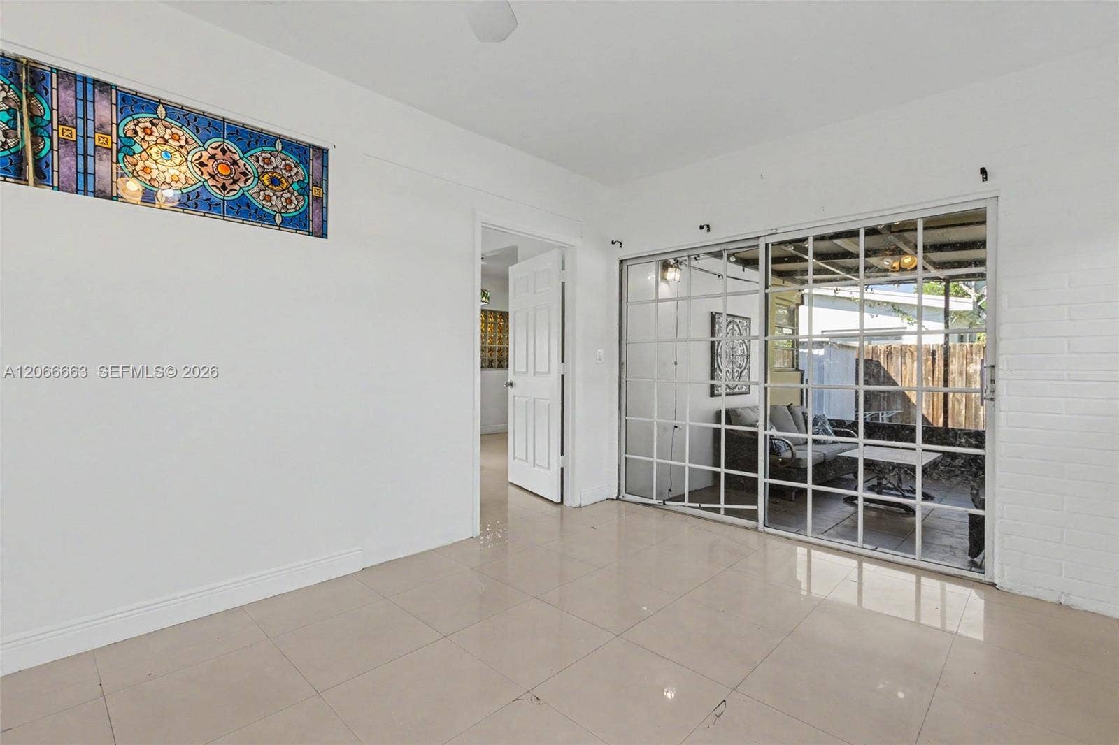 1191 NE 175th Street, North Miami Beach, FL 33162 Interior space featuring large-format tile flooring, decorative stained-glass transom window, white-painted brick wall, and multi-pane sliding glass doors