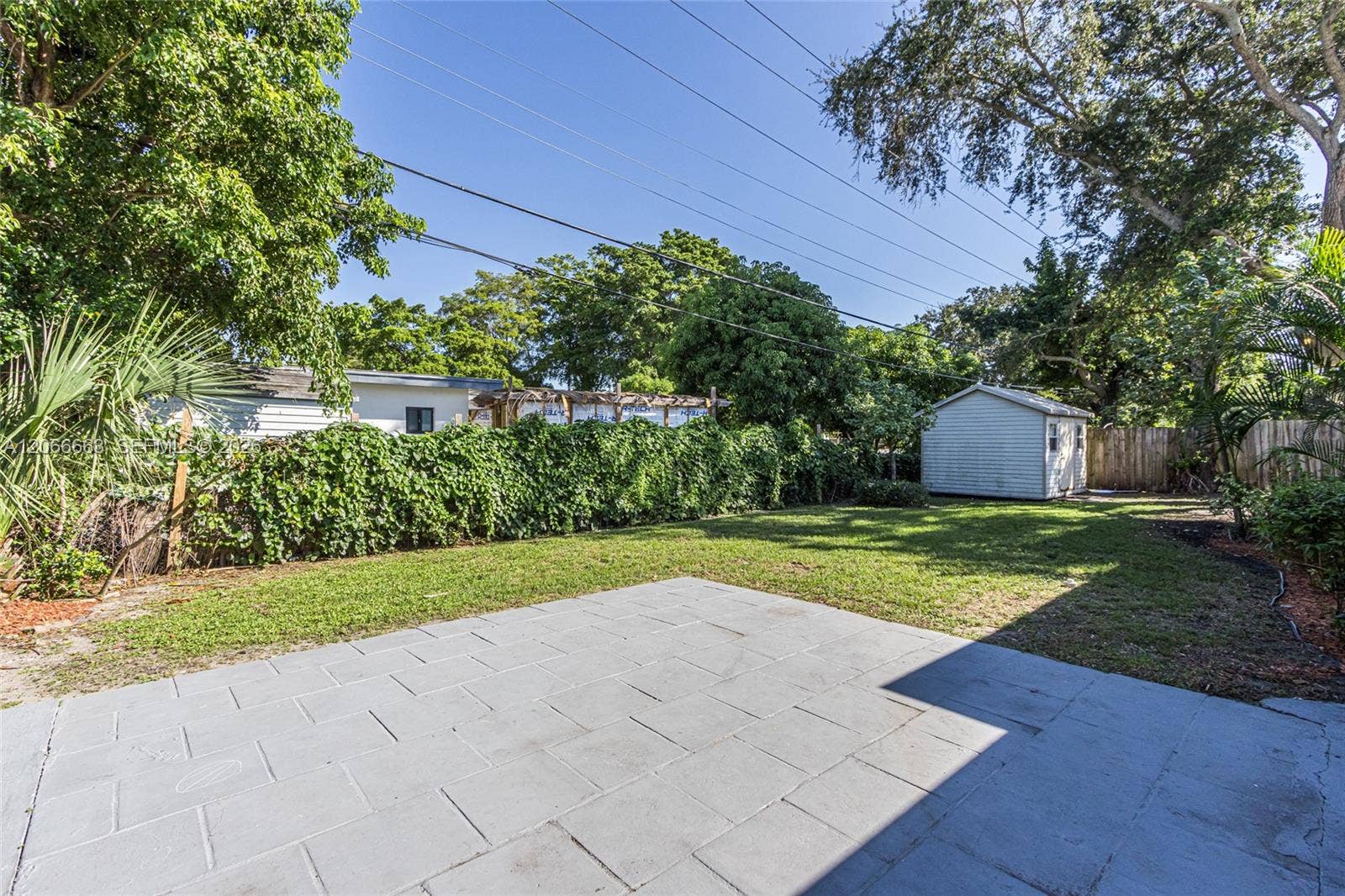 1191 NE 175th Street, North Miami Beach, FL 33162 Backyard featuring a paved patio, grass lawn, detached storage shed, and mature trees