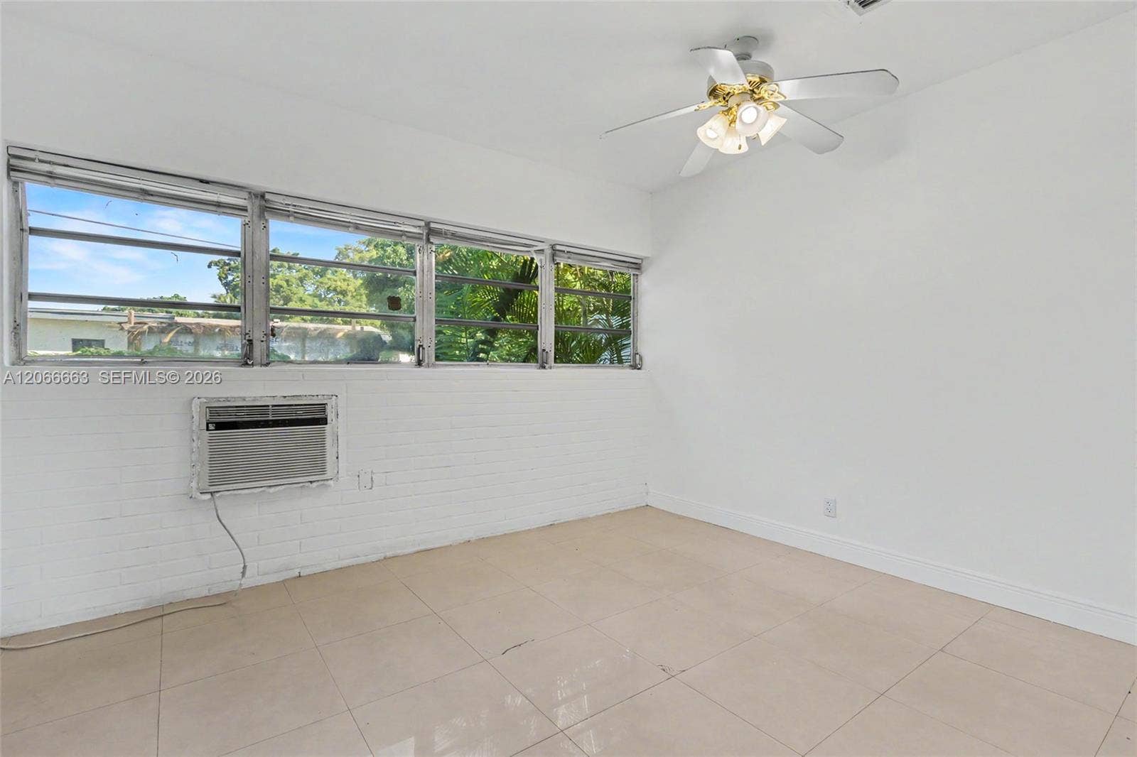 1191 NE 175th Street, North Miami Beach, FL 33162 Room featuring white painted brick walls, neutral tile flooring, multi-pane casement windows, and a ceiling fan with integrated lighting