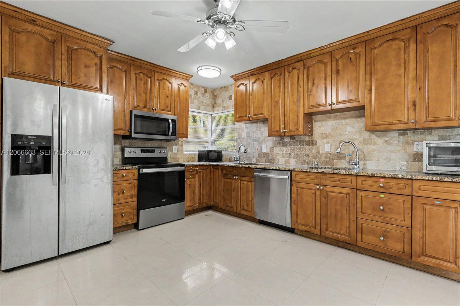 1191 NE 175th Street, North Miami Beach, FL 33162 Kitchen featuring extensive wood cabinetry, stone-tiled backsplash, polished stone countertops, stainless steel appliances, and large-format tile flooring