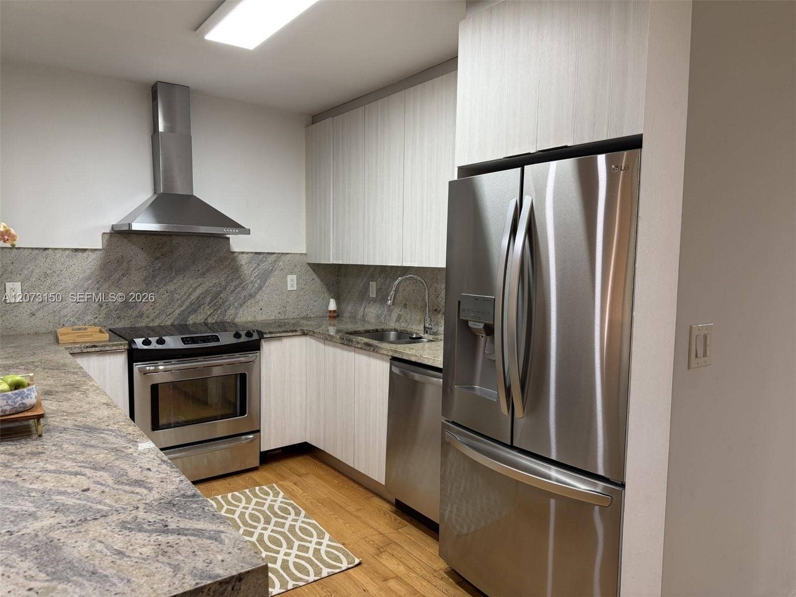 141 Crandon Boulevard, #243, Key Biscayne, Key Biscayne, FL 33149 Kitchen featuring flat-panel cabinetry, stone countertops, stainless steel appliances, a mounted range hood, and wood-finish flooring