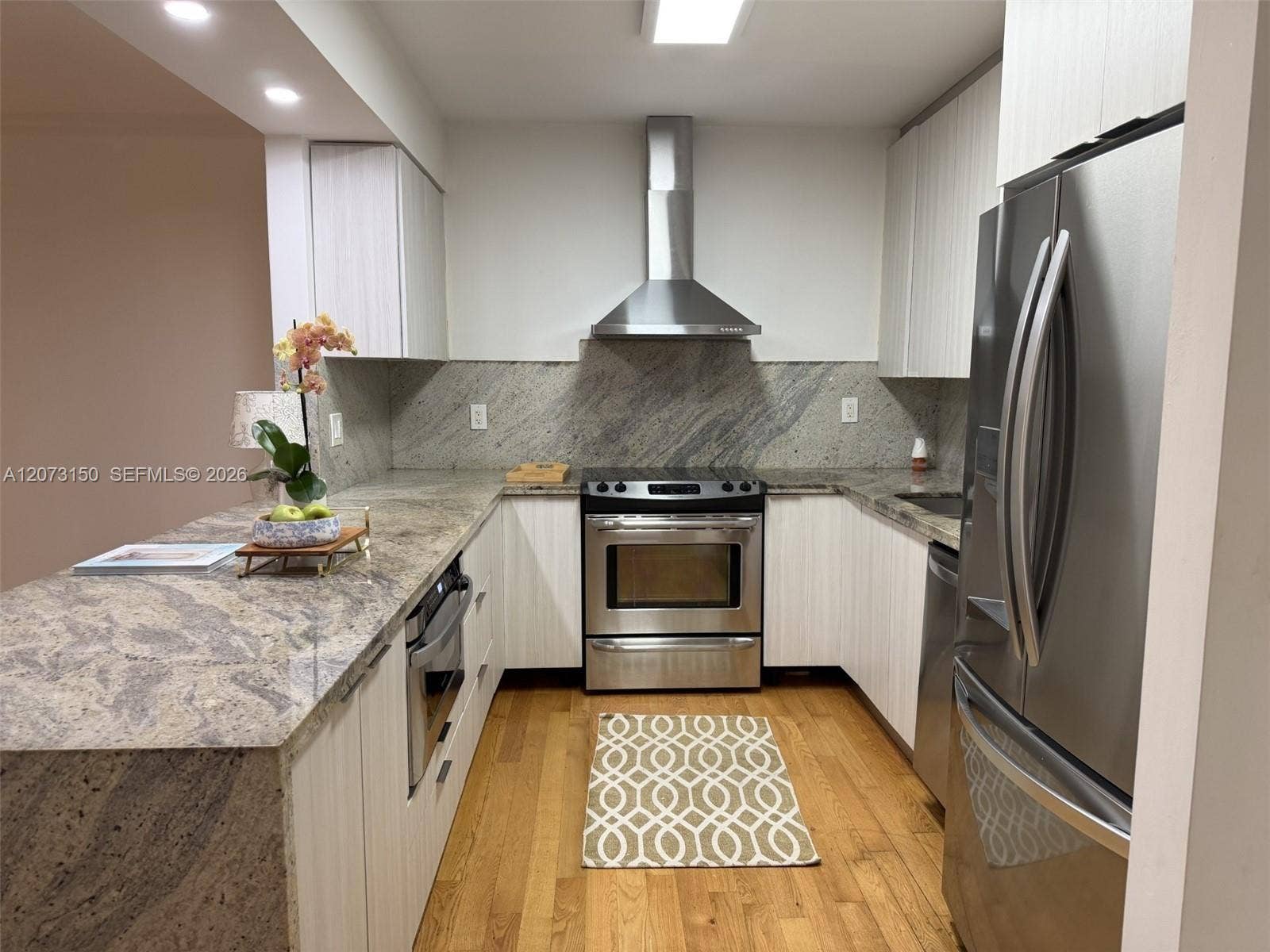 141 Crandon Boulevard, #243, Key Biscayne, Key Biscayne, FL 33149 Kitchen featuring stone countertops, white vertical-grain cabinetry, stainless steel appliances, a chimney-style range hood, and wood-finish flooring