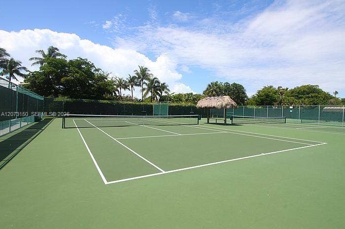 141 Crandon Boulevard, #243, Key Biscayne, Key Biscayne, FL 33149 Private tennis court featuring a hard surface, perimeter chain-link fencing with wind-screen paneling, and a thatched-roof palapa structure