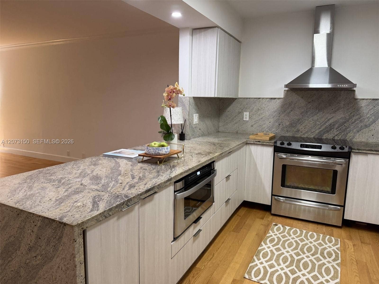 141 Crandon Boulevard, #243, Key Biscayne, Key Biscayne, FL 33149 Kitchen featuring flat-panel cabinetry, stone countertops, stainless steel appliance suite, chimney-style range hood, and wood-finish flooring