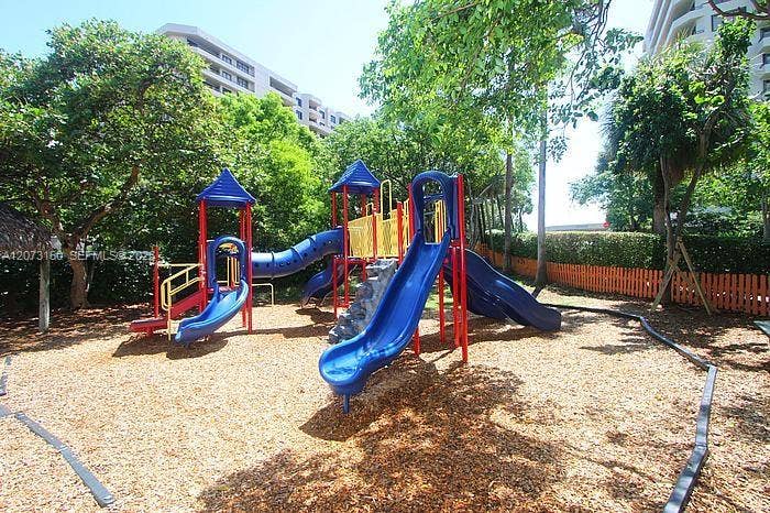 141 Crandon Boulevard, #243, Key Biscayne, Key Biscayne, FL 33149 Outdoor play area featuring multi-level slides, a tunnel attachment, climbing structure, wood chip ground cover, and mature shade trees