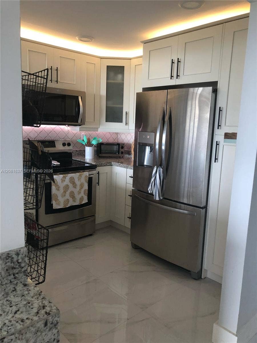 8233 Harding Avenue, #707, Miami Beach, Miami Beach, FL 33141 White cabinetry featuring glass-panel accents, stainless steel appliances, patterned tile backsplash, polished stone-finish flooring, and recessed ceiling lighting