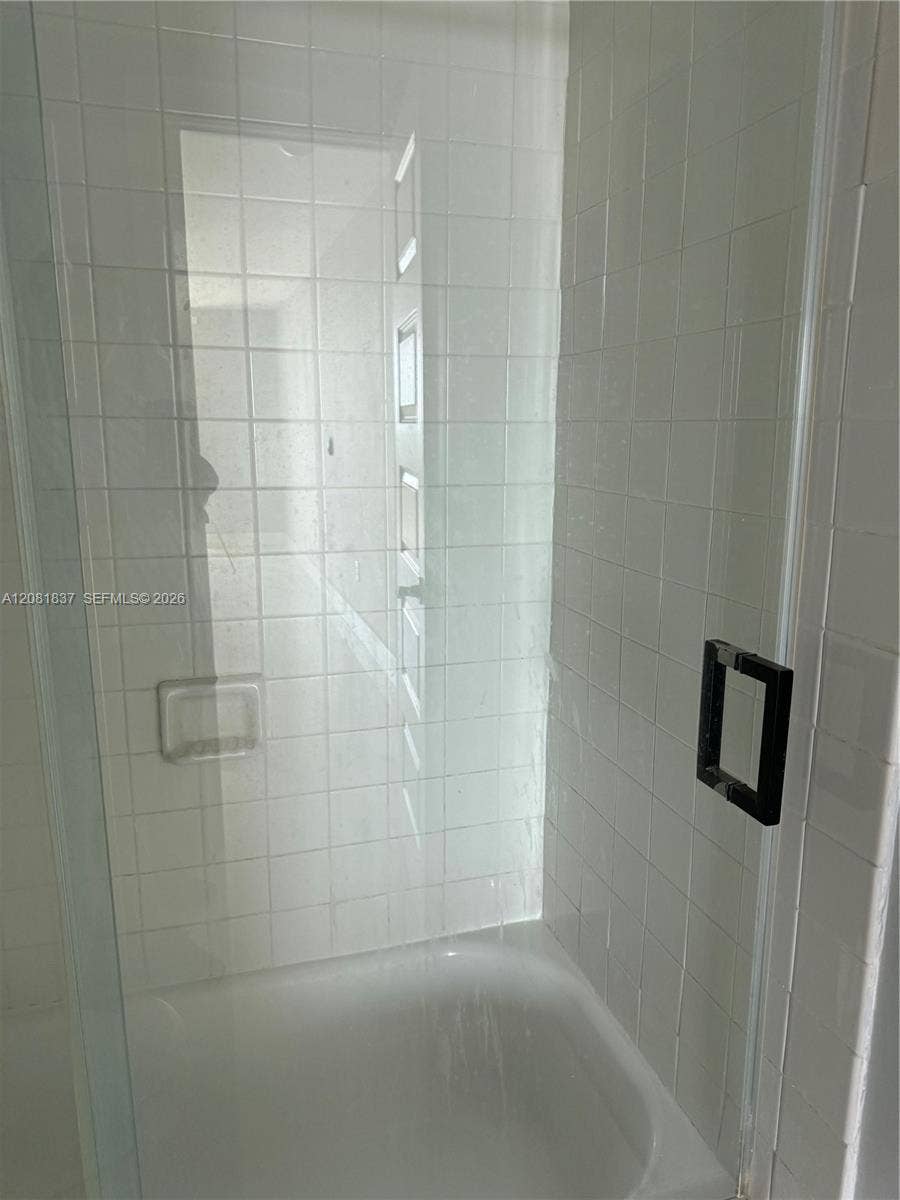 8233 Harding Avenue, #707, Miami Beach, Miami Beach, FL 33141 Shower enclosure featuring floor-to-ceiling white square tile, a built-in recessed soap niche, a frameless glass door, and a matte black square handle