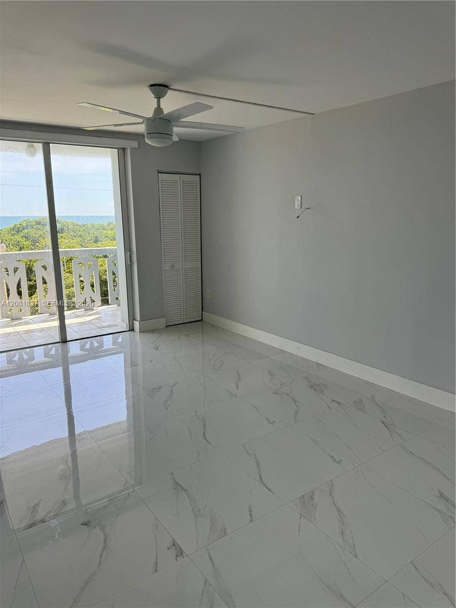 8233 Harding Avenue, #707, Miami Beach, Miami Beach, FL 33141 Polished large-format tile flooring with a marble-finish, white louvered closet door, ceiling fan with integrated lighting, and glass sliding doors opening to a balcony with an ocean backdrop
