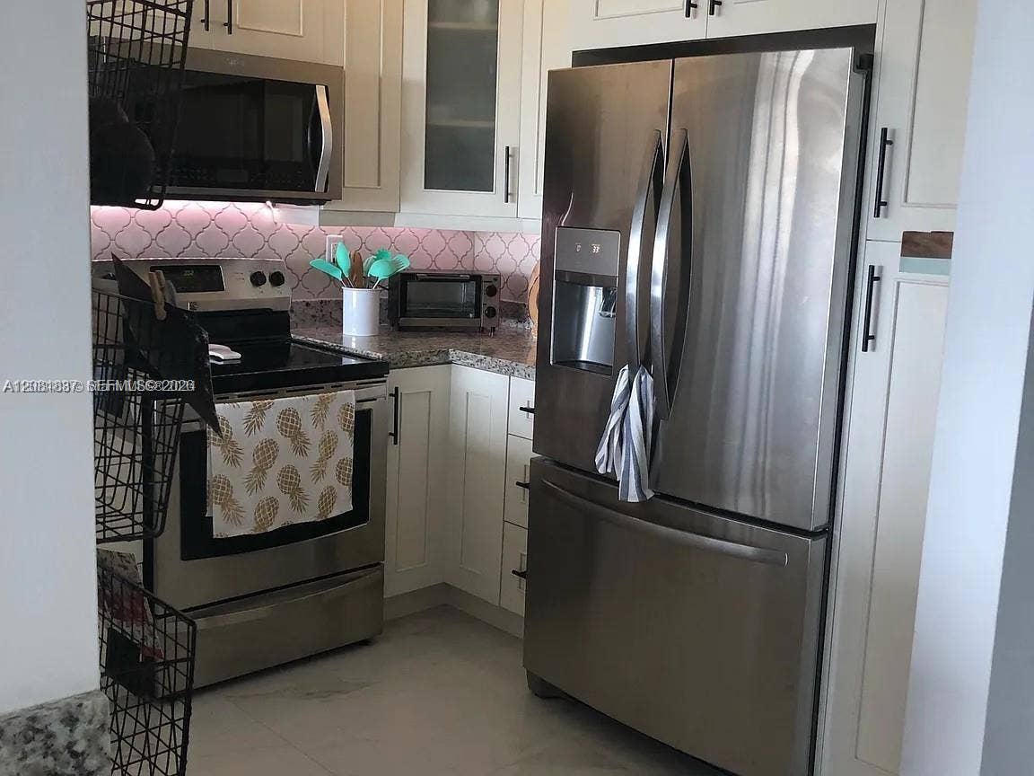 8233 Harding Avenue, #707, Miami Beach, Miami Beach, FL 33141 Kitchen featuring white shaker-style cabinetry, stainless steel appliances, speckled stone-finish countertops, patterned tile backsplash, and under-cabinet lighting