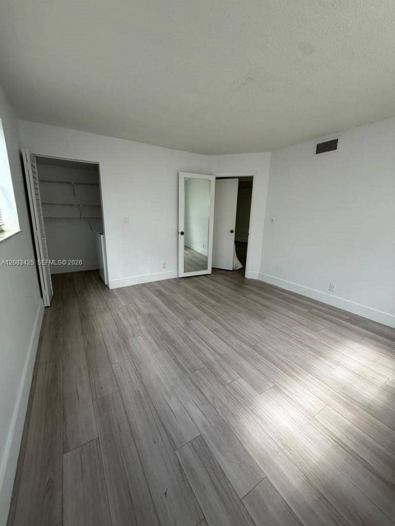 8001 Fairview Drive, #101, Tamarac, Tamarac, FL 33321 Room featuring wood-finish flooring, a walk-in closet with built-in shelving, and a door with a full-length integrated mirror