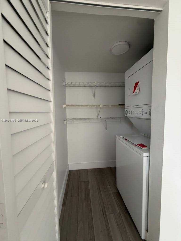 8001 Fairview Drive, #101, Tamarac, Tamarac, FL 33321 Laundry closet featuring louvered bi-fold doors, wood-finish flooring, stacked laundry appliance, and three levels of built-in wire shelving