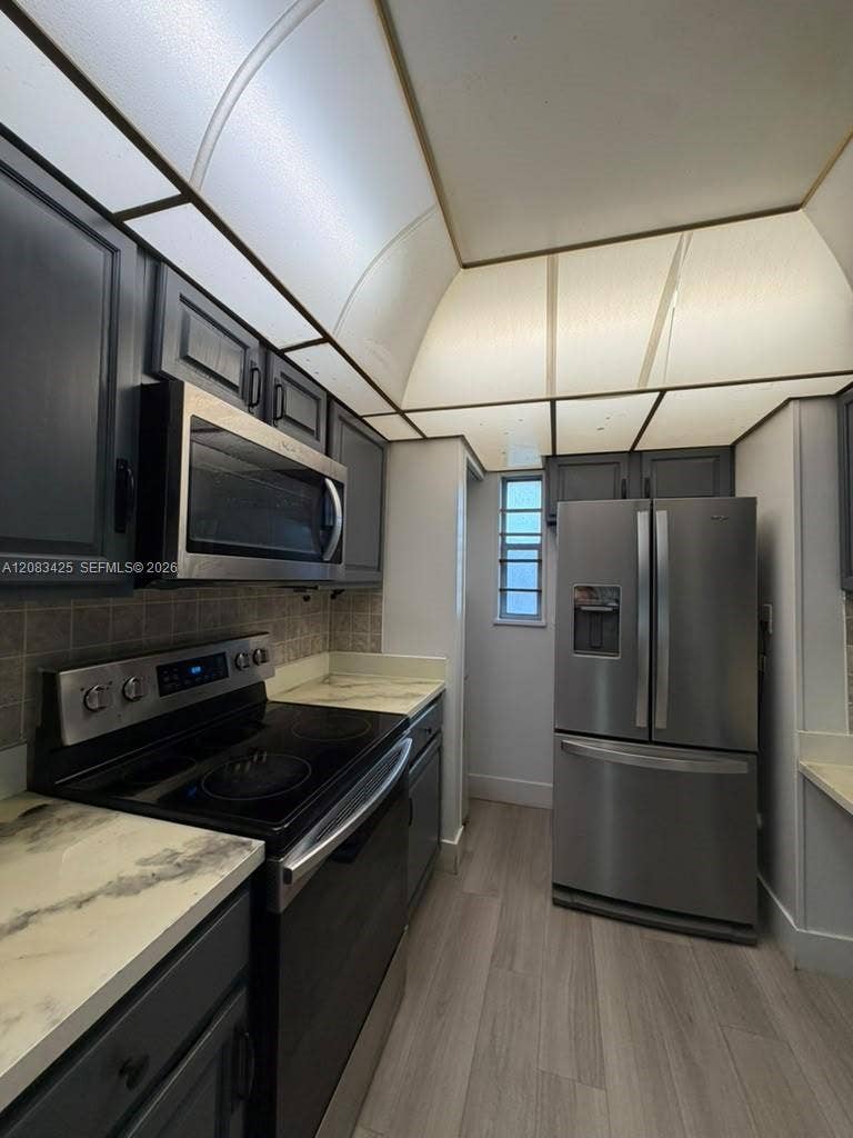 8001 Fairview Drive, #101, Tamarac, Tamarac, FL 33321 Kitchen featuring dark-toned cabinetry, light-toned countertops with a marble-patterned finish, wood-finish flooring, and stainless steel appliances