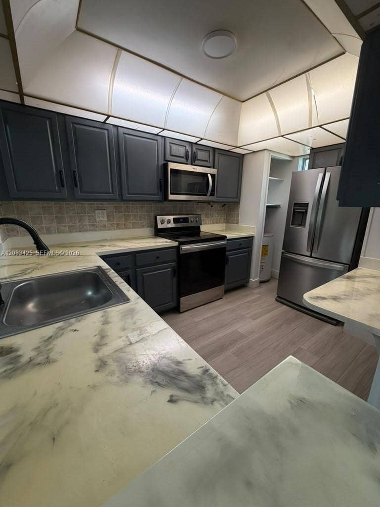 8001 Fairview Drive, #101, Tamarac, Tamarac, FL 33321 Kitchen featuring dark-toned cabinetry, stainless steel appliances, patterned countertops, wood-finish flooring, and a tray ceiling with recessed lighting