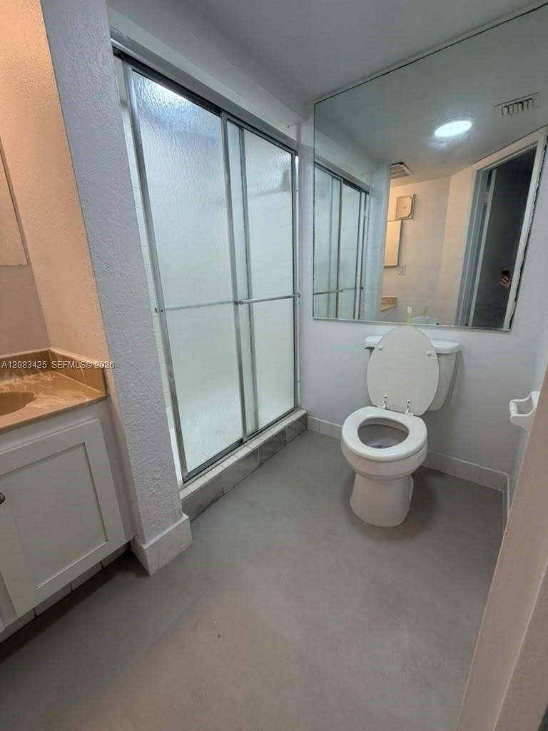 8001 Fairview Drive, #101, Tamarac, Tamarac, FL 33321 Bathroom featuring a walk-in shower with a sliding glass enclosure, white cabinetry, a neutral-toned countertop, and an expansive wall-mounted mirror