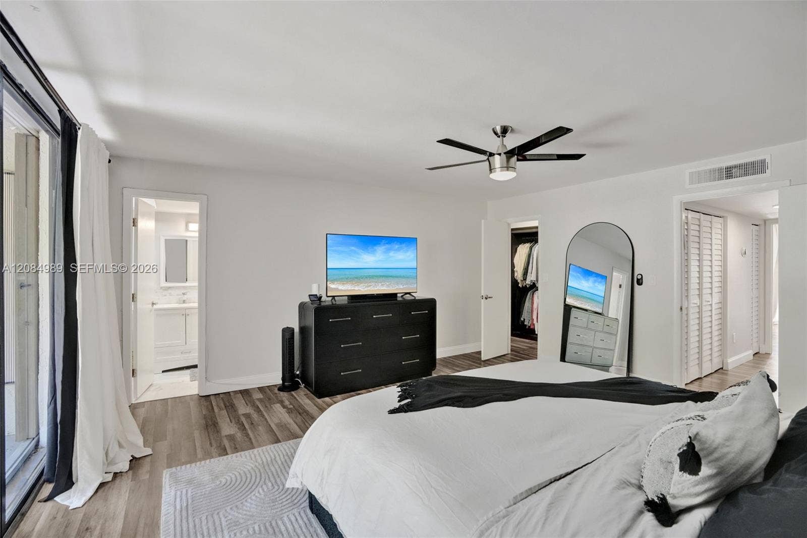 Neutral-toned wood-finish flooring, brushed metal ceiling fan, and louvered closet doors