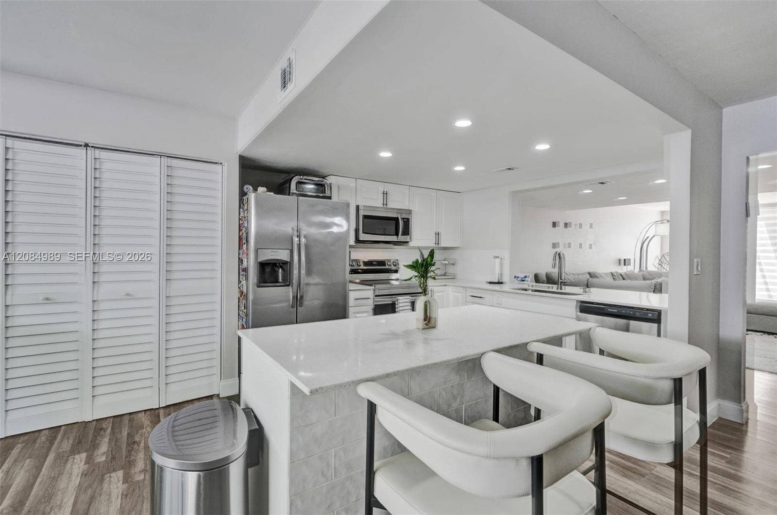 Kitchen featuring a stone-surface island, stainless steel appliances, white cabinetry, recessed lighting, and wood-finish flooring