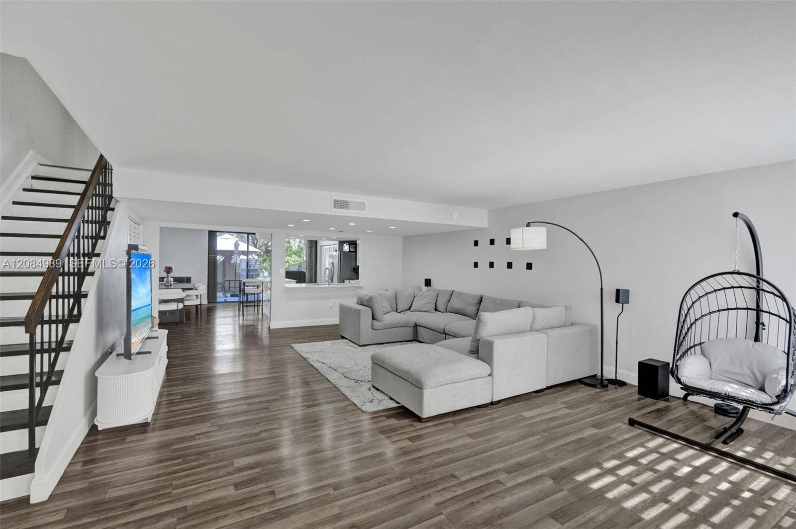 Open-concept living space featuring wood-finish flooring, recessed lighting, and a staircase with a metal railing and wood handrail