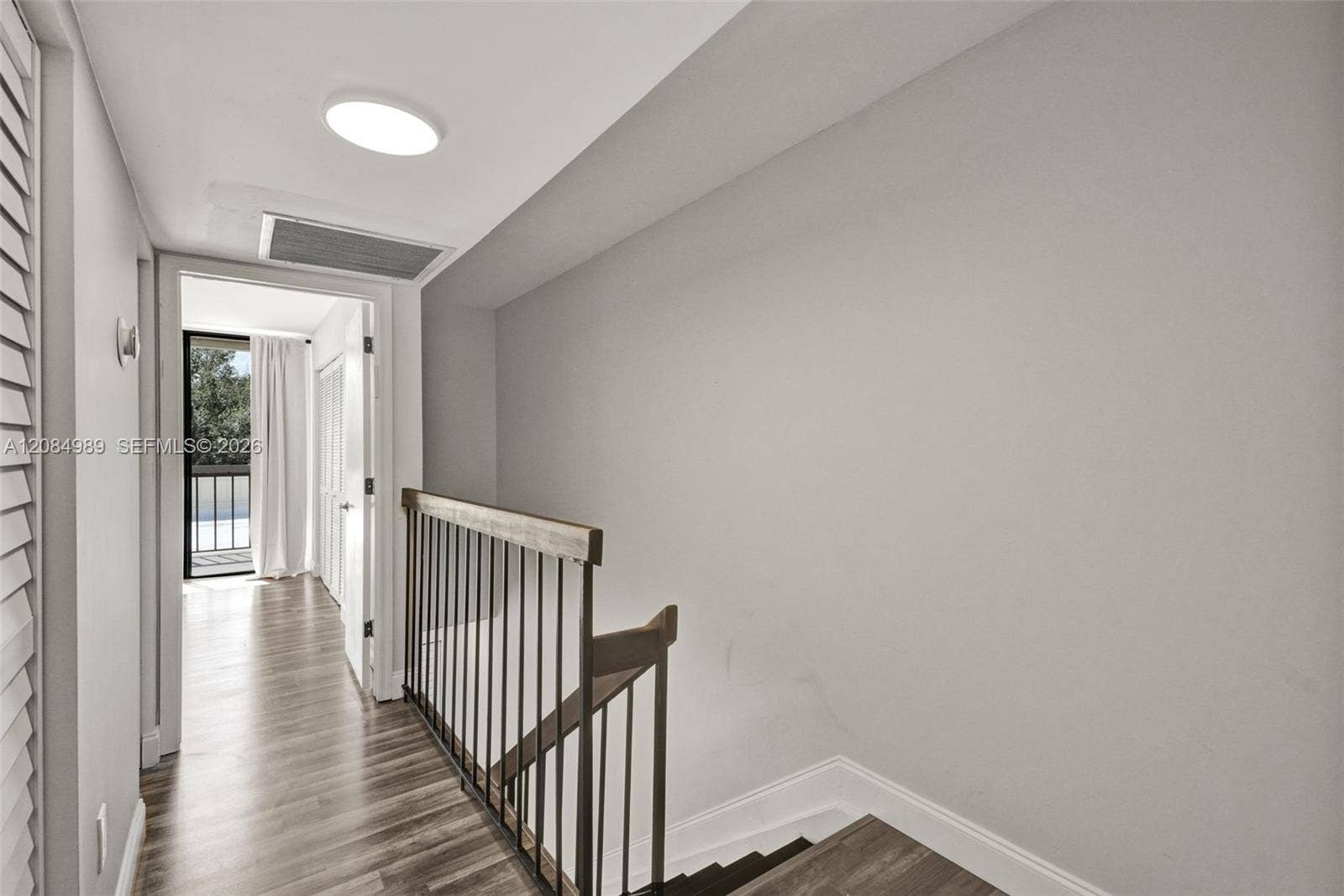 Wood-finish flooring, staircase featuring a dark-toned handrail, and metal balusters