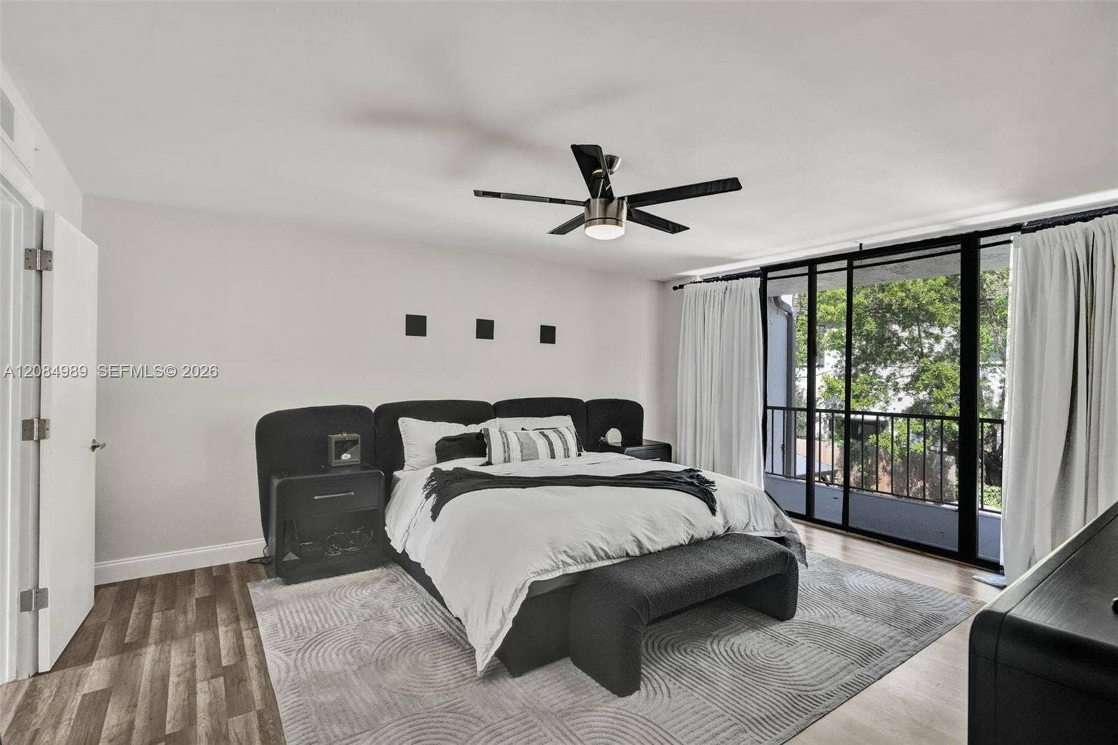 Room featuring wood-finish flooring, a matte black multi-blade ceiling fan with integrated lighting, and floor-to-ceiling sliding glass doors opening to a private balcony