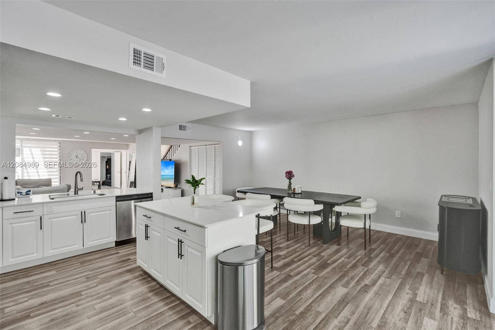 Kitchen featuring a central island with a solid surface countertop, white shaker-style cabinetry, stainless steel dishwasher, undermount sink with a gooseneck faucet, and wood-finish flooring