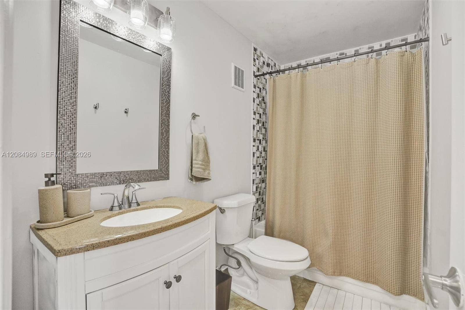 Bathroom featuring a white vanity cabinet, solid-surface countertop with an integrated basin, mosaic-tiled mirror frame, three-light fixture, and a tile-surround shower area