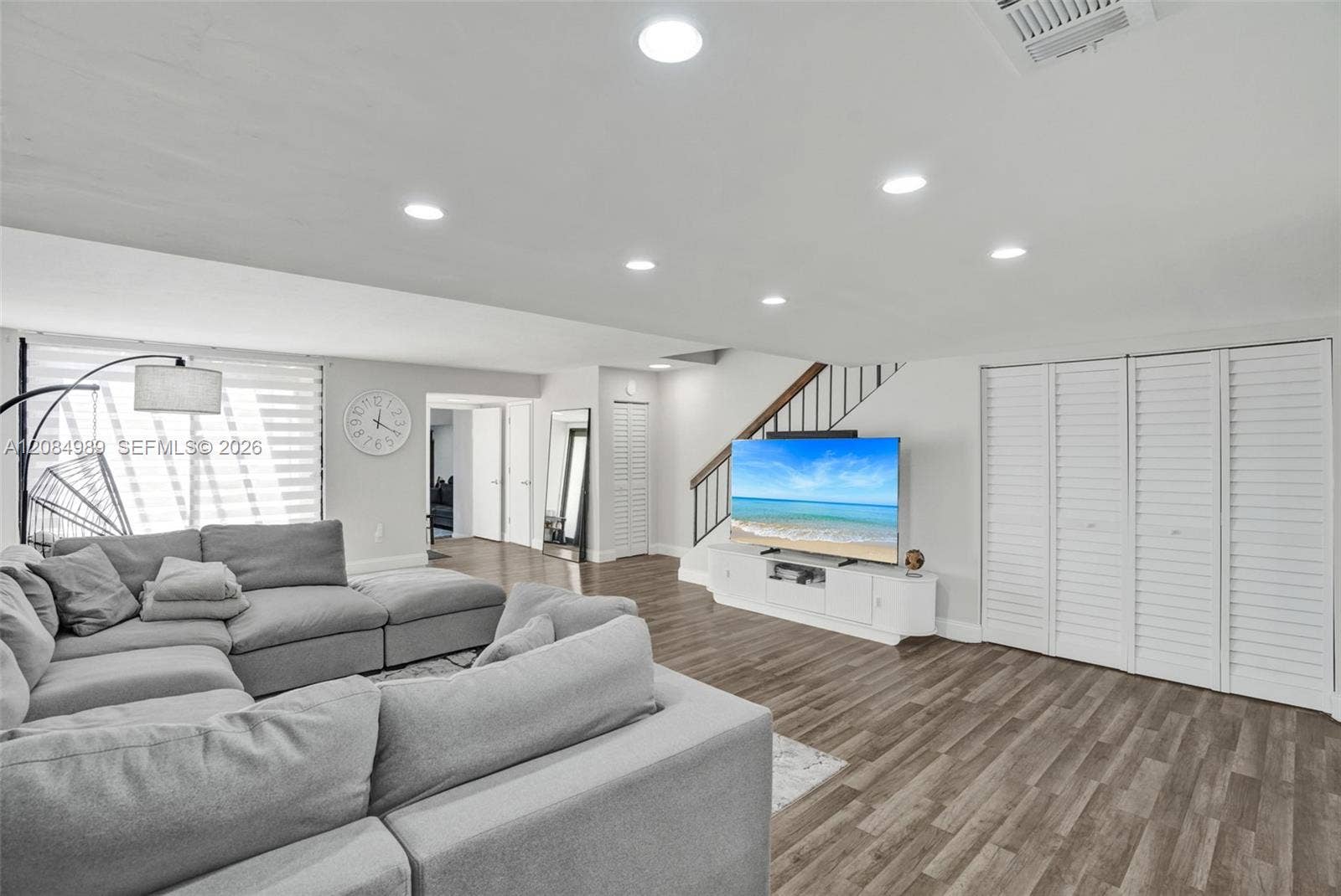Living area featuring wood-finish flooring, recessed lighting, multi-panel louvered closet doors, and a staircase with a wooden handrail and metal balusters