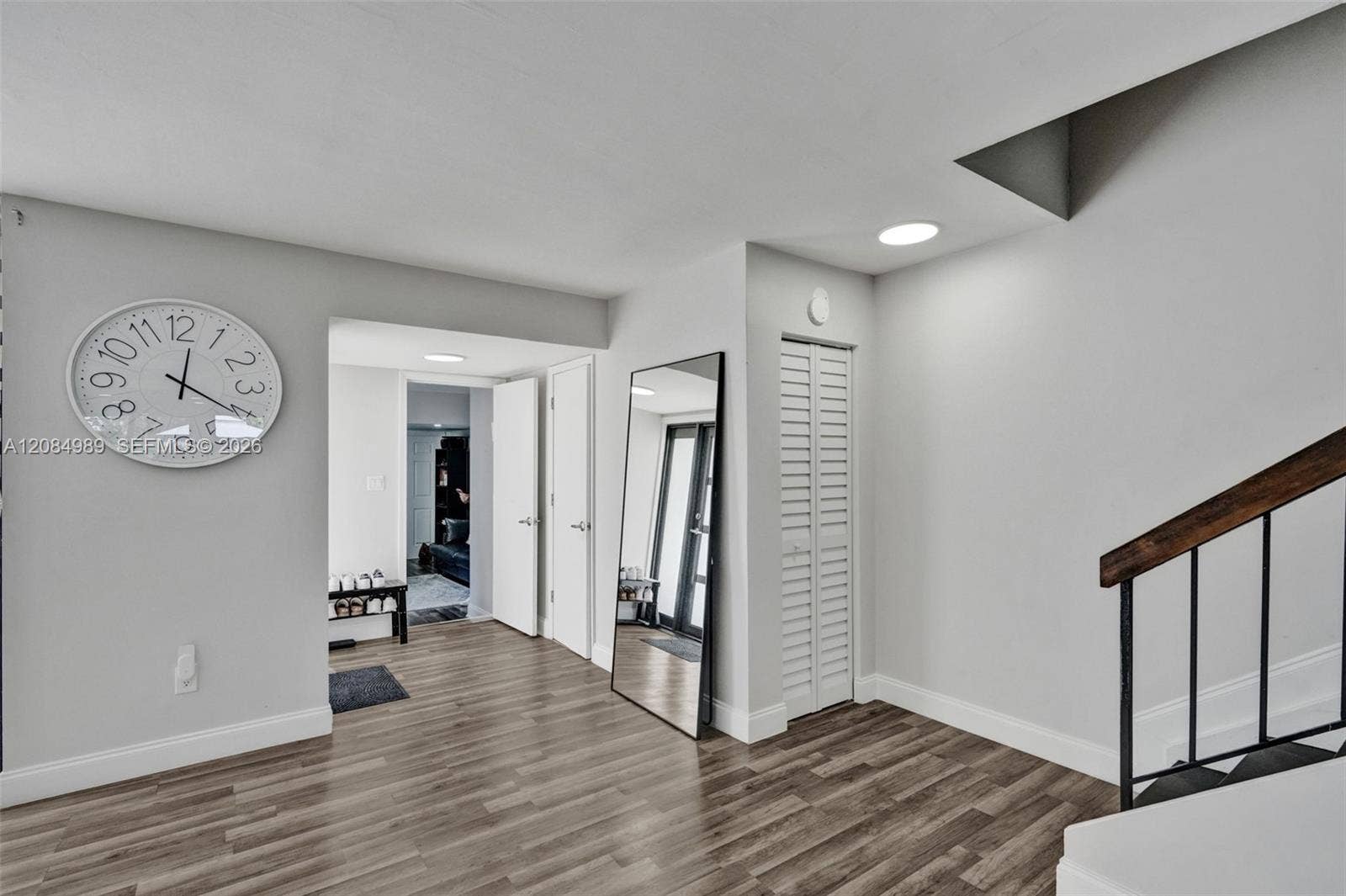 Wood-finish flooring, white louvered-door closet, and staircase featuring a dark metal railing with a wood handrail