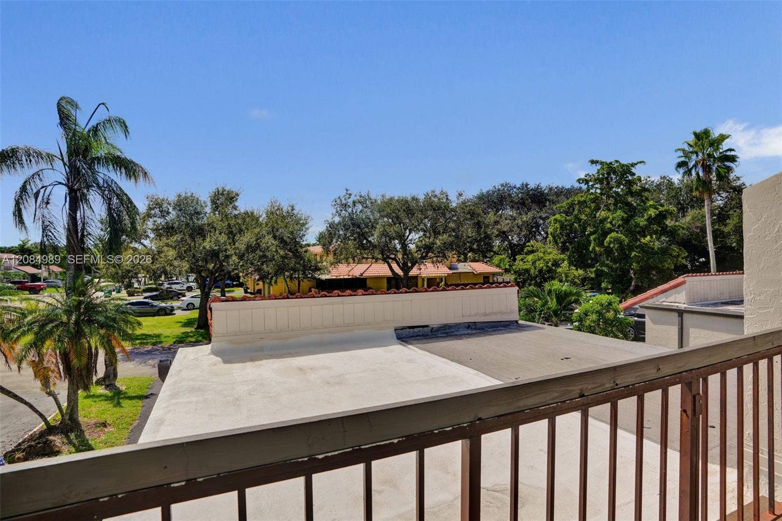 Elevated balcony with metal railing featuring mature palm trees and established landscaping