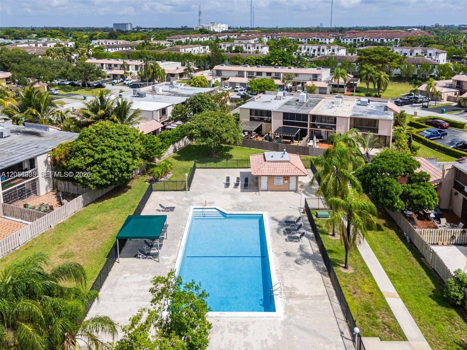Community swimming pool featuring a concrete deck, a covered seating area, a detached structure with a tile roof, and perimeter fencing