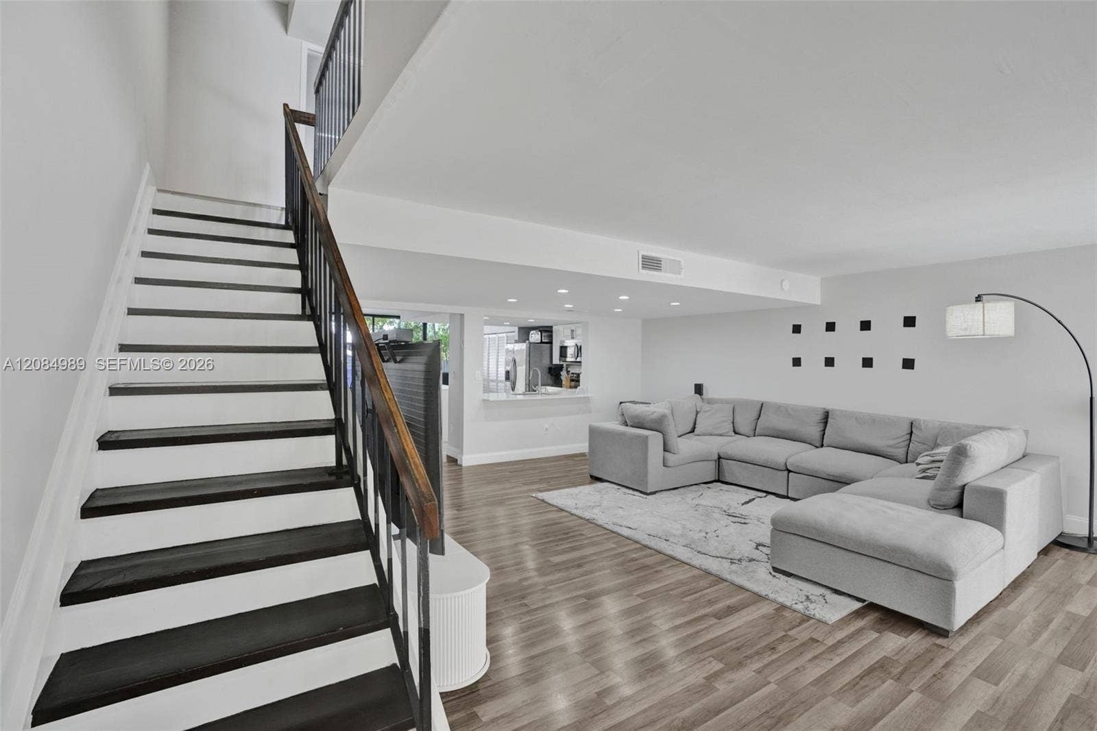 Staircase featuring dark-stained treads and a wrought-iron railing, wood-finish flooring, recessed lighting, and a service pass-through window with a quartz-style ledge
