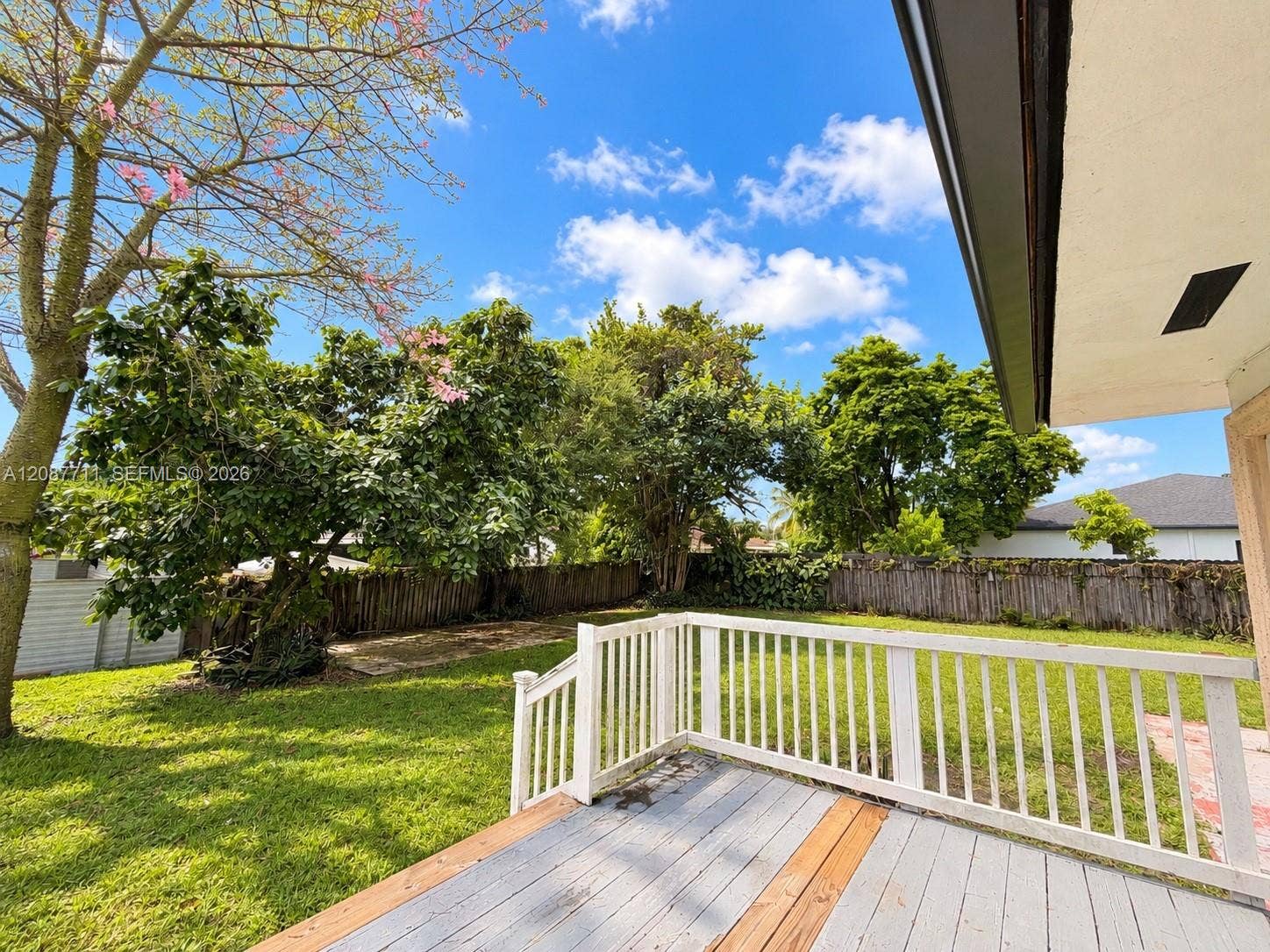 80 NE 162nd Street, Miami, Miami, FL 33162 Backyard featuring a raised wooden deck with white railing, lawn area, and mature trees enclosed by a privacy fence