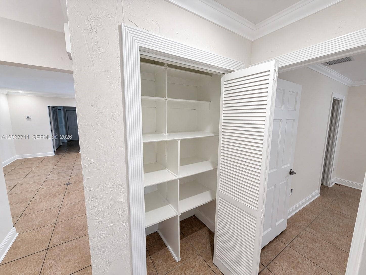 80 NE 162nd Street, Miami, Miami, FL 33162 Built-in storage closet featuring custom shelving, louvered white door, decorative door casing, and tile flooring