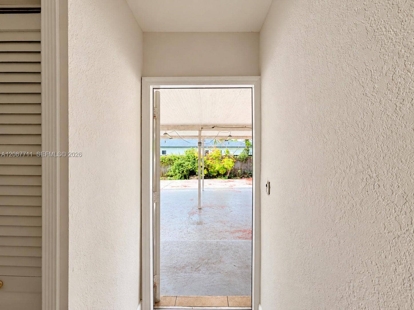 80 NE 162nd Street, Miami, Miami, FL 33162 Entryway featuring louvered bi-fold closet doors and a glass-paneled exterior door opening to a concrete patio with a covered structure